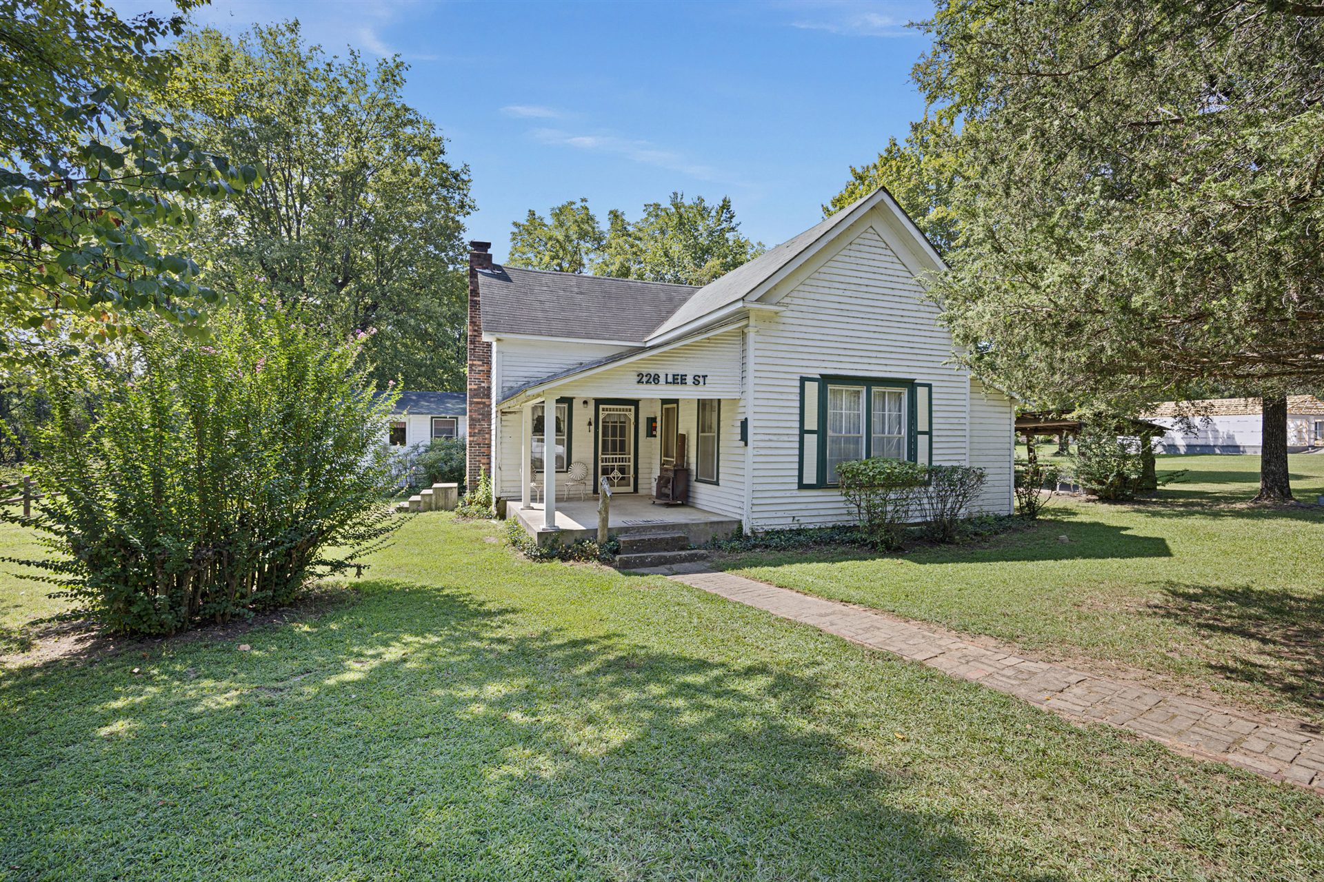Existing white farmhouse at 226 Lee Street, with a covered front porch, green shutters and mature shade trees